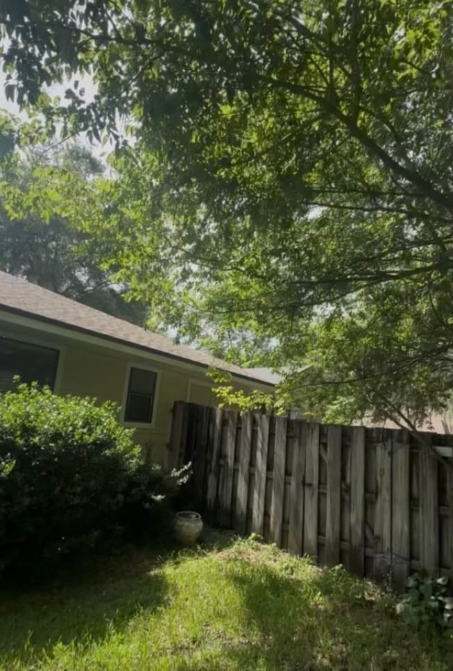 Before — a side yard along a wood privacy fence, tree limbs hanging low and a shrub spilling out over the grass.